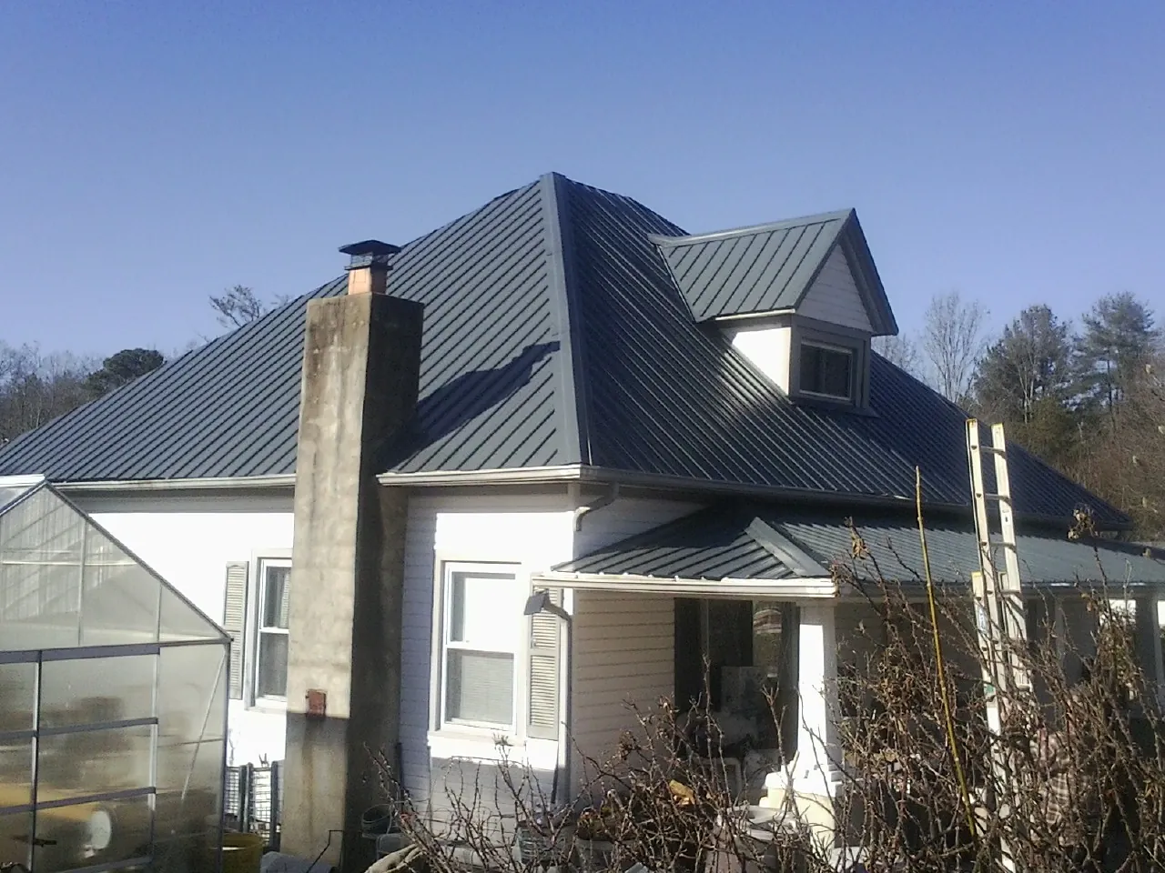 Dark blue standing seam metal roof on a white farmhouse with dormer — Slate & Tile Roof Repair by Roofing Brothers in Mount Laurel