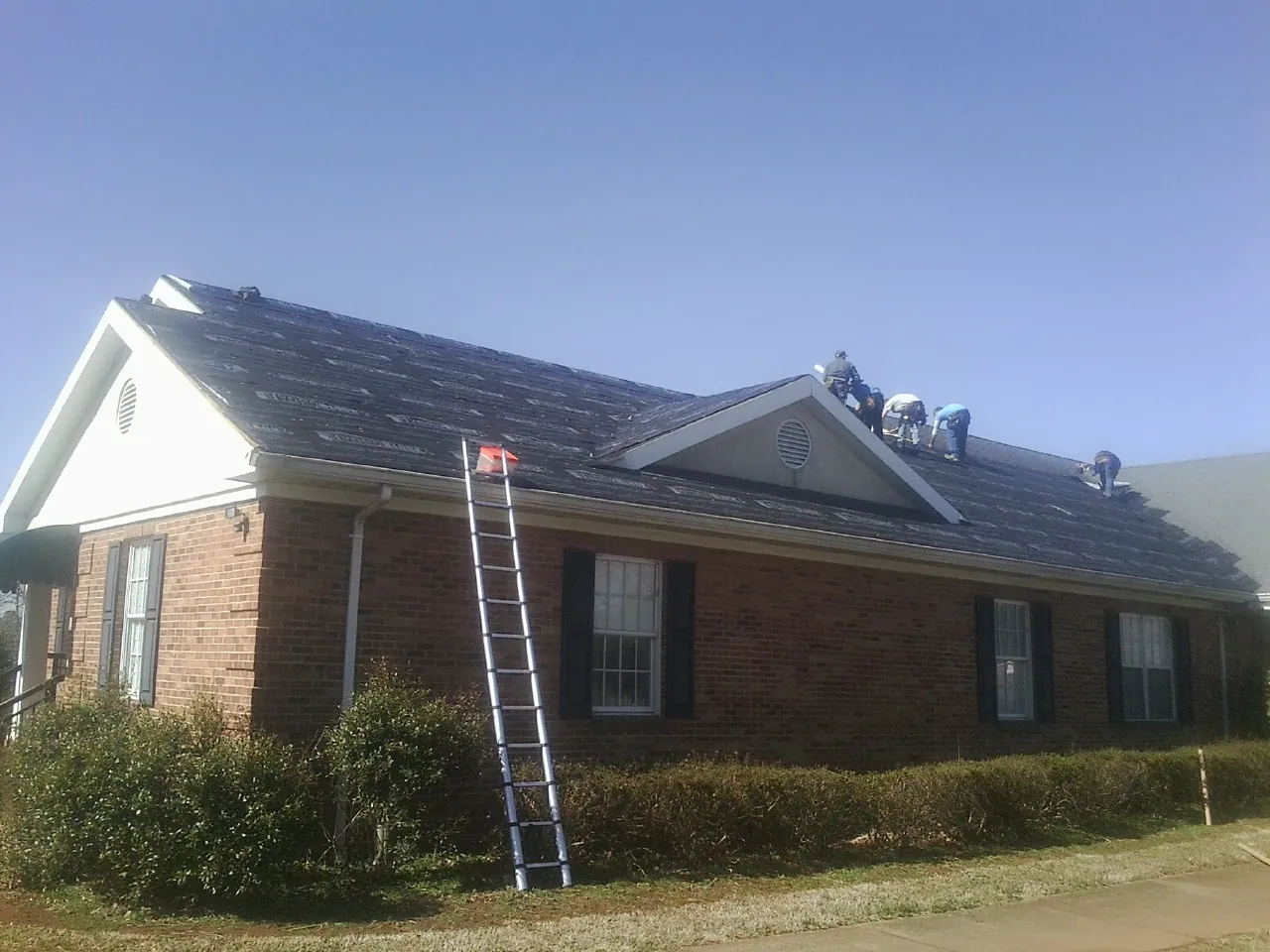 Crew tearing shingles off a brick ranch roof with a ladder set — Emergency Roof Repair work by our crew in Mount Laurel