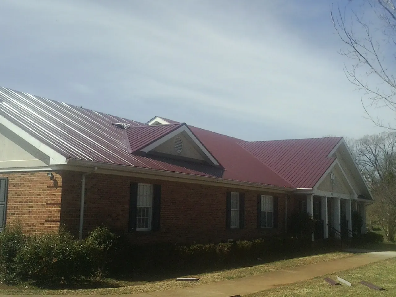 Red metal roof with gabled entries on a long brick building, from a Hail Damage Roof Repair job in Mount Laurel