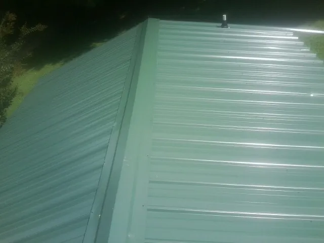 New green metal panels meeting at the ridge of a roof — Flat Roof Repair work by our crew in Mount Laurel