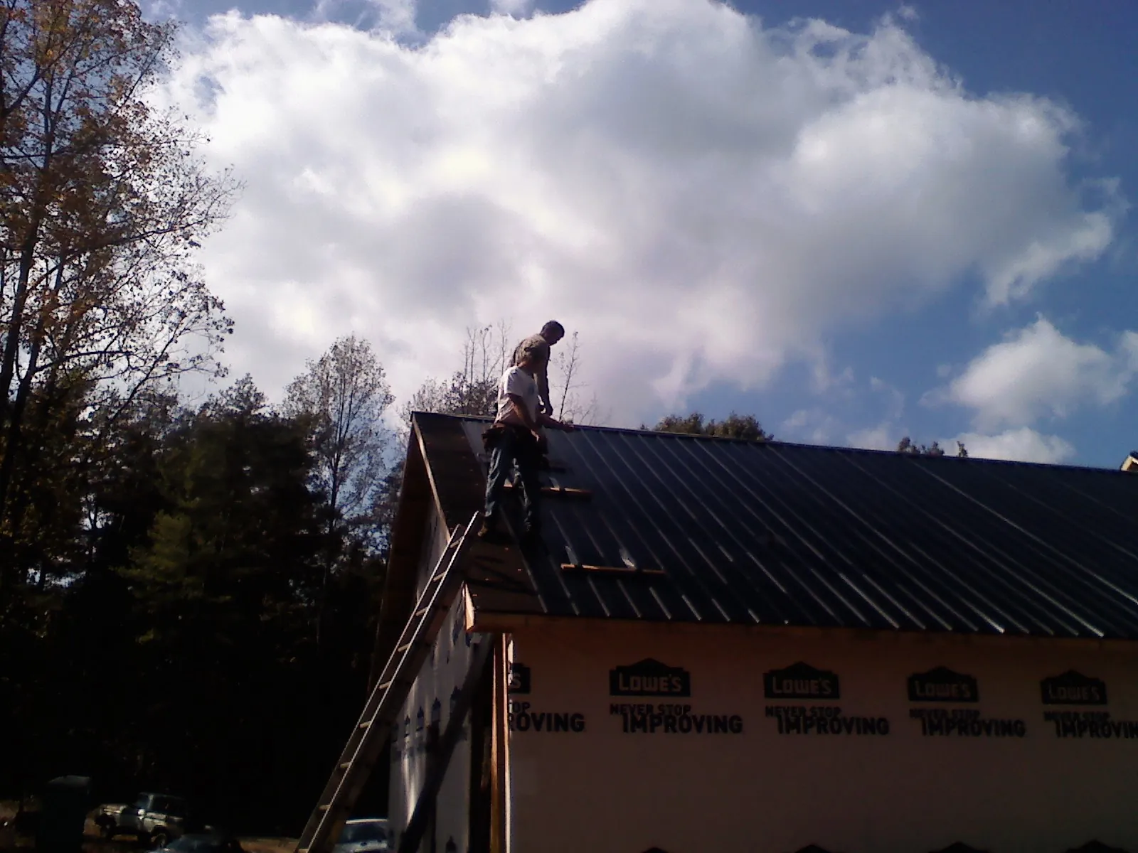 Roofer fastening dark metal panels high against a cloudy sky, from a Roof Inspection job in Mount Laurel